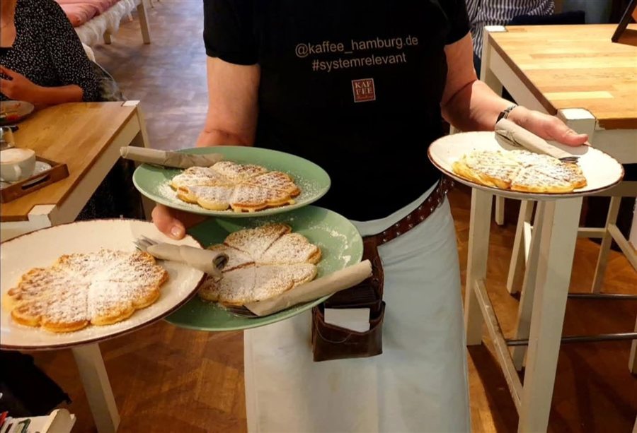 Drei Teller mit frischen Waffeln und Puderzucker werden zum Tisch getragen.