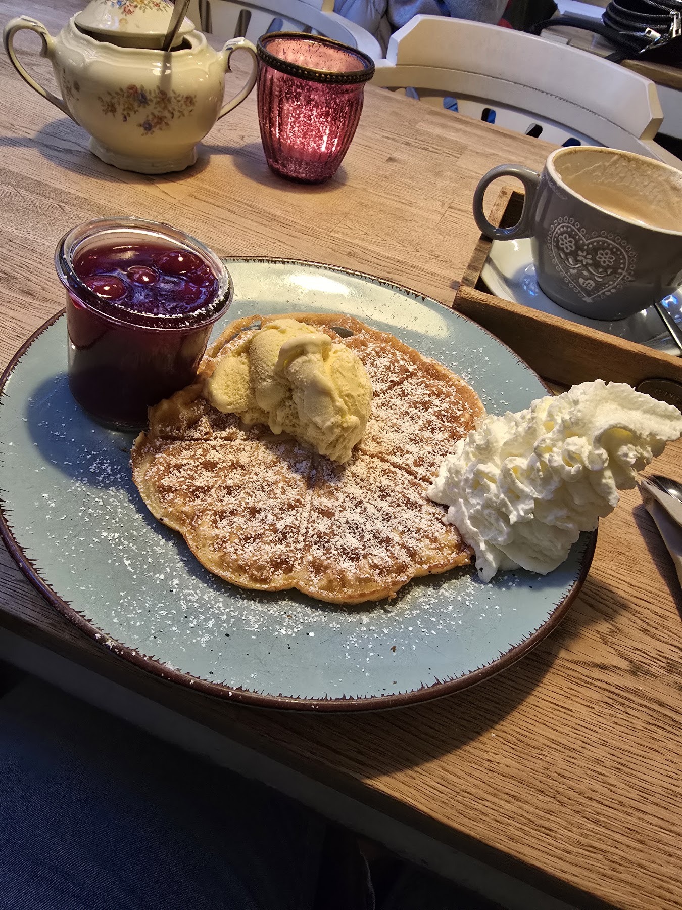 Waffel mit Puderzucker, einer Kugel Vanilleeis, Sahne und einem Glas heißer Kirschen.